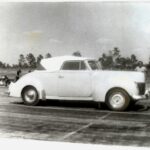         Description: A black and white photo of a car on a drag racing track.