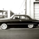 A black and white photo of a car parked in front of a gas station at a drag racing event.