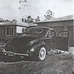 A black and white photo of an old car parked in front of a house.