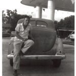 A man leaning against a car at a gas station, possibly connected to drag racing.