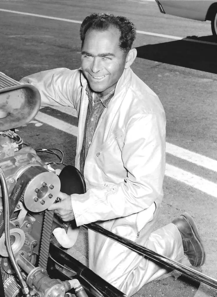 A man passionately kneels beside a car engine, immersed in the world of drag racing.