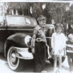 Three children standing in front of an old car used for drag racing.