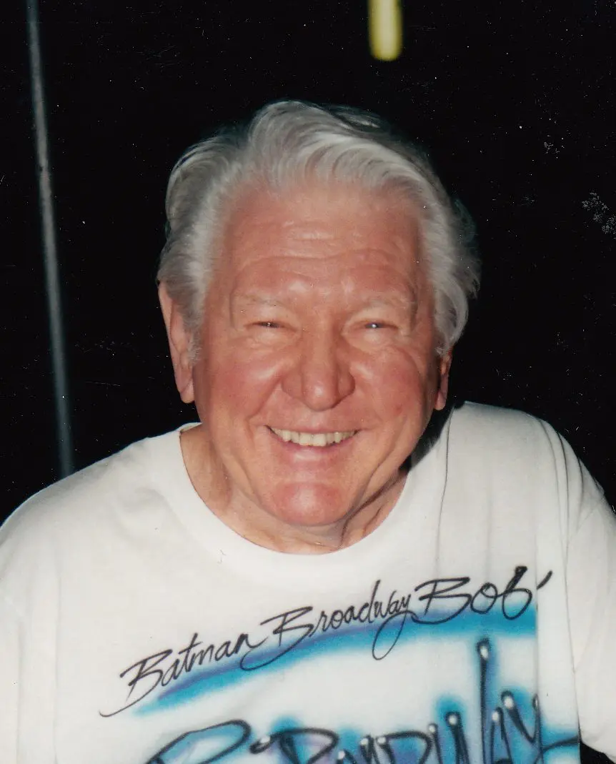 An older man participating in drag racing, wearing a white t-shirt and smiling.