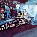 A man is drag racing, driving a car with smoke coming out of it.
