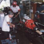 Two men engaged in drag racing working on a car in a garage.