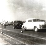 A vintage photo capturing the thrill of drag racing with a group of cars on a drag strip.