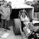 A group of people standing around a drag racing car.