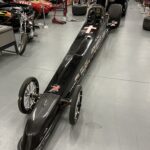 A black dragster, built for the exhilarating world of drag racing, sits in a garage.