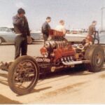 A group of people standing next to a drag car at a drag racing event.