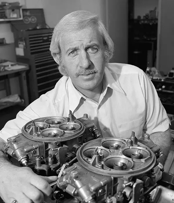 A drag racing enthusiast proudly holds two carburetors in front of him.