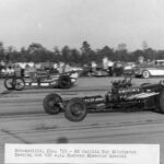 A black and white photo of a drag car racing on a track.