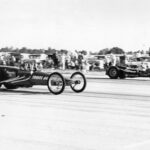 A black and white photo of two drag racing cars speeding on a track.