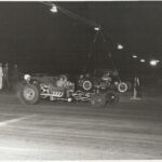 A exhilarating black and white photo of a race car speeding through the night in a thrilling drag racing event.