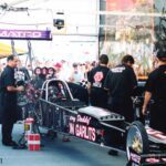 A group of men standing around a drag car at a drag racing event.