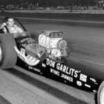 A black and white photo of a man drag racing.