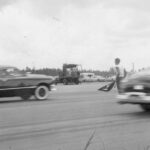A black and white photo of a man drag racing in a car.