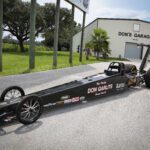 A black drag car parked in front of a garage, ready for some high-speed drag racing.