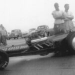 A group of men standing next to a drag car at a Drag Racing event.