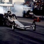 A drag racer speeding down a track with smoke billowing from its exhaust.