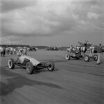 A black and white photo of a drag racing car on the tarmac.