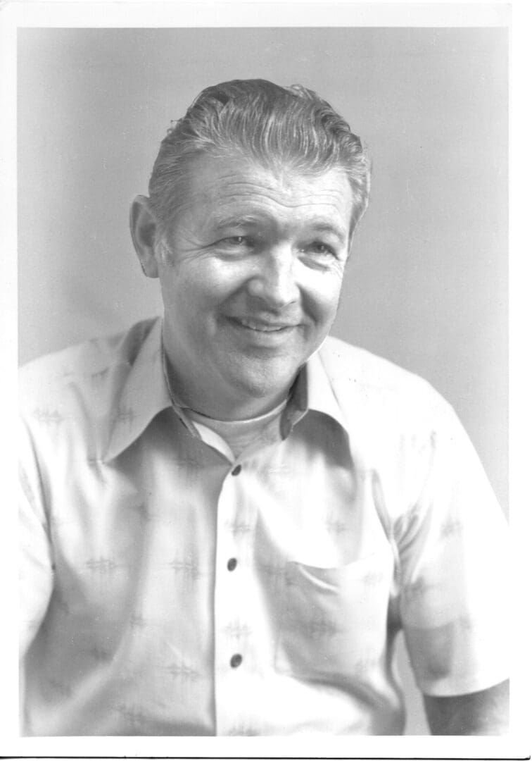 A black and white photo of a man smiling at a drag racing event.