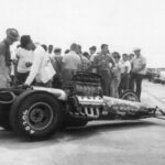 A group of people standing around a drag car at a drag racing event.