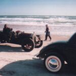 An old car participating in a drag racing event parked on the beach.