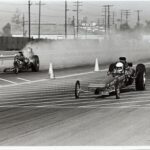Two drag racers competing on a track, emitting plumes of smoke from their hoods in the thrilling world of drag racing.