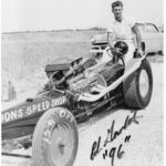 An old photo of a man standing next to a race car at a drag racing event.