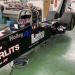 A sleek black race car, perfect for drag racing, is sitting in a garage.