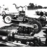 An old photo of a race car parked in a parking lot, showcasing drag racing history.