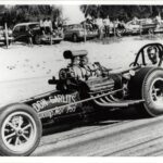 A black and white photo capturing the exhilaration of drag racing as a man confidently drives his powerful car down the track.