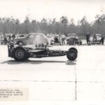 An old photo capturing the exhilaration of drag racing with a skilled man behind the wheel of a powerful drag car.