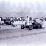 An old photo of a drag race with a man driving a car capturing the exhilarating world of Drag Racing.