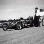 A man is standing next to a car at a drag racing event.