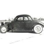 A vintage black and white photo of an old car from the era of drag racing.