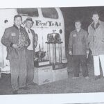 Four men standing in front of a truck with drag racing trophies.