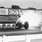A black and white photo of a drag racing car with smoke coming out of it.