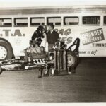 A man and a dog standing next to a bus at a Drag Racing event.