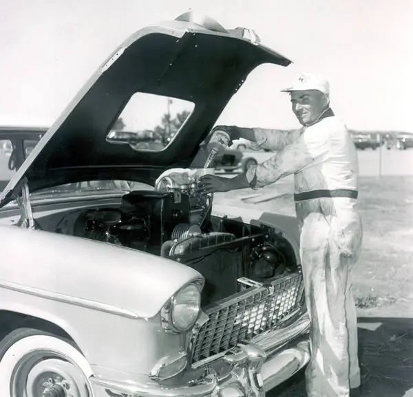 A man, specialized in drag racing, meticulously working on the engine of an old car.