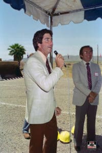 Man speaking at outdoor event under tent.