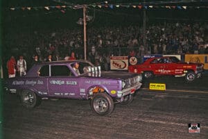 Two vintage drag racing cars at night.