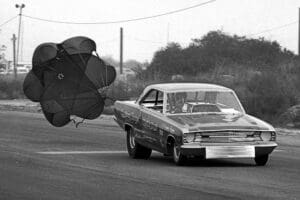 Drag racing car deploying parachute on track.