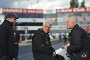 Three men talking at a racetrack event.