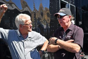 Two men talking beside a black vehicle.