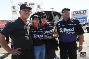 Racing team posing with a trophy outdoors.