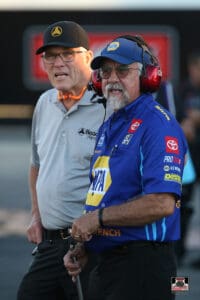 Two men standing, one wearing headphones.