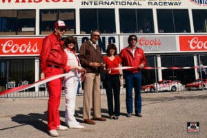 Group cutting ribbon at racetrack event.