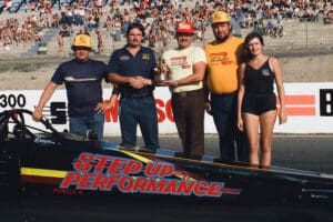 Drag racing team with trophy and car.