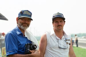 Two men wearing caps, outdoors, smiling.